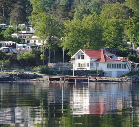 Bild av Anfasteröd Gårdsvik: Ett charmigt hus vid vattnet med en lantlig känsla. Området präglas av en lugn vattenström och omgivande natur, vilket skapar en idyllisk miljö. I bakgrunden syns delar av en liten by.