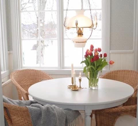 Ett smakfullt inrett rum på Anfasteröd Gårdsvik med träbord och stolar, elegant belysning inklusive en kristallkrona i taket och ett trägolv som skapar en varm och inbjudande atmosfär.