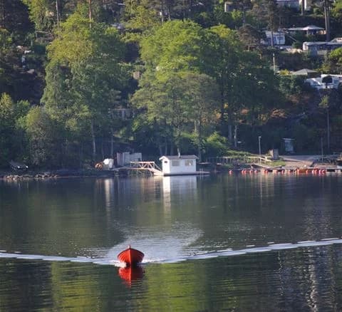 En lugn vattenyta med flera båtar förtöjda vid en brygga, omgiven av grönskande natur, vid Anfasteröd Gårdsvik.