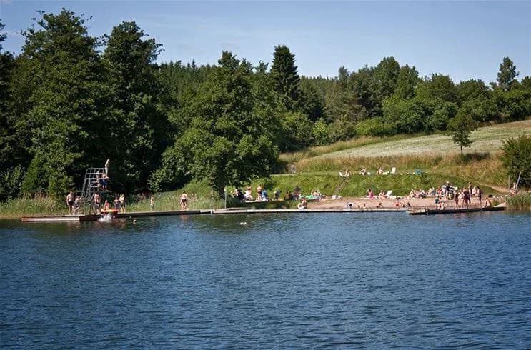 En bild av Yxningens camping med en naturskön sjövy. På bilden syns en brygga som leder ut i vattnet, omgiven av grönskande natur. Perfekt för avkoppling och rekreation under semestern.