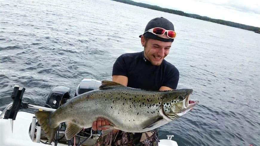 En person fiskar vid Yxningens camping, omgiven av lugnt vatten och grönska.