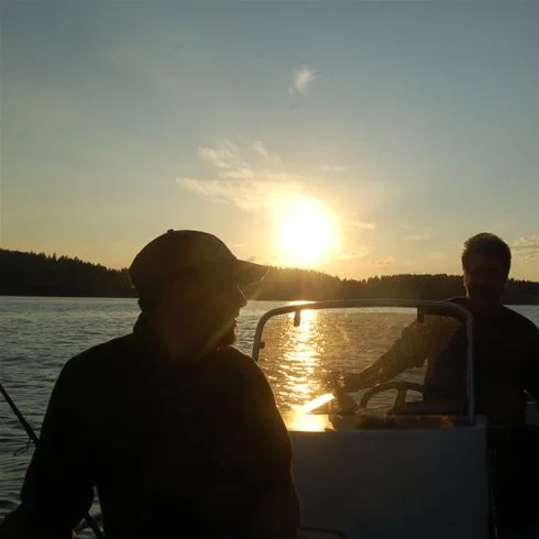 En båt ligger förtöjd vid stranden vid Yxningens camping under en vacker solnedgång, där vattnet i sjön skimrar i det mjuka kvällsljuset.