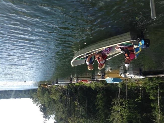 En motorbåt ligger förtöjd vid en brygga i en stilla sjö, omgiven av rogivande natur vid Yxningens camping. Vattnet speglar båten och den omkringliggande skogen.