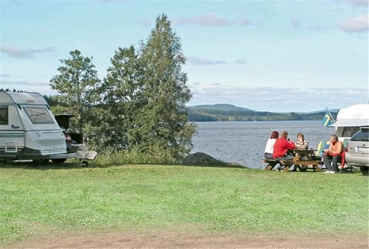 En campingplats vid Munkebergs camping, med tält och husvagnsfordon uppställda i ett parkliknande område, omgiven av naturskön miljö i närheten av sjödistriktet.