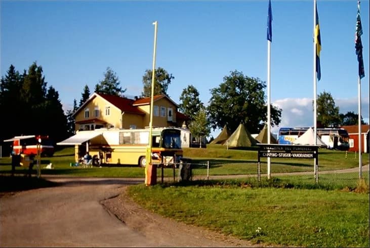 En campinglplats med grönt gräs och tält, omgiven av träd och en flaggstång, i Munkebergs Camping.