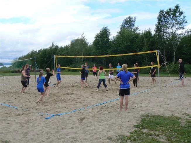 En grupp människor spelar volleyboll utomhus på Storstrand kursgård, med ett volleybollnät tydligt synligt i bakgrunden, omgiven av natur och sommarklädda deltagare.