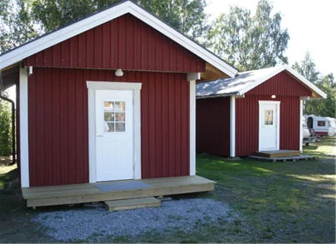 Bild av Storstrand kursgård som visar en stuga omgiven av en välskött gräsmatta och trädgård. Trähusets sidoklädsel är i gott skick och omgivningen präglas av lummiga trädsilhuetter och en öppen tomt.