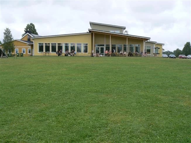 En stor grön gräsyta på Storstrand kursgård, med öppna fält och träd, lämplig för rekreation och sportaktiviteter.