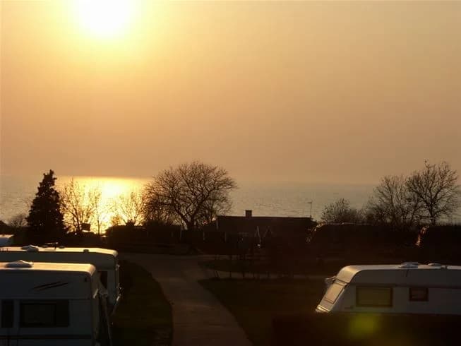 En stämningsfull bild av Klinta Camping under skymningen, där solen sakta går ner och himlen fylls av mjuka färger i gult och rosa.