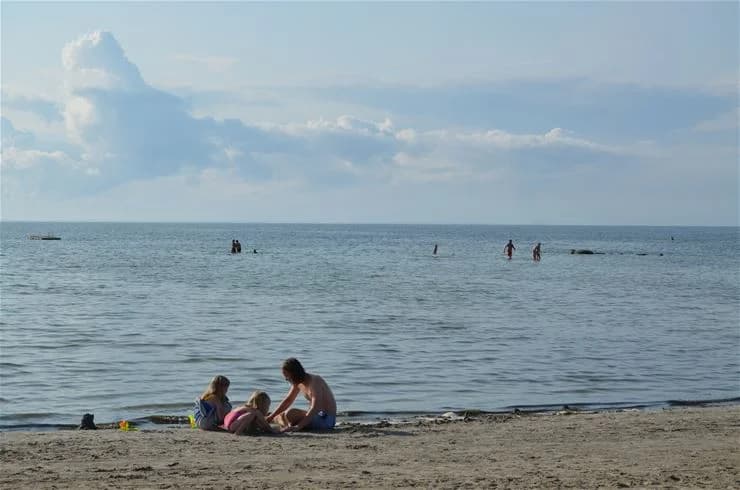 En sandstrand vid Klinta Camping med vågor som slår mot stranden en solig sommardag. Havet sträcker sig mot horisonten, och människor njuter av sin semester i det sköna vädret.