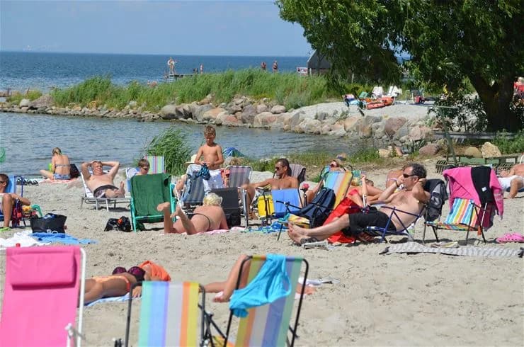 En solig stranddag på Klinta Camping med människor som njuter av sommarens rekreation och avkopplar vid havets kustlinje.