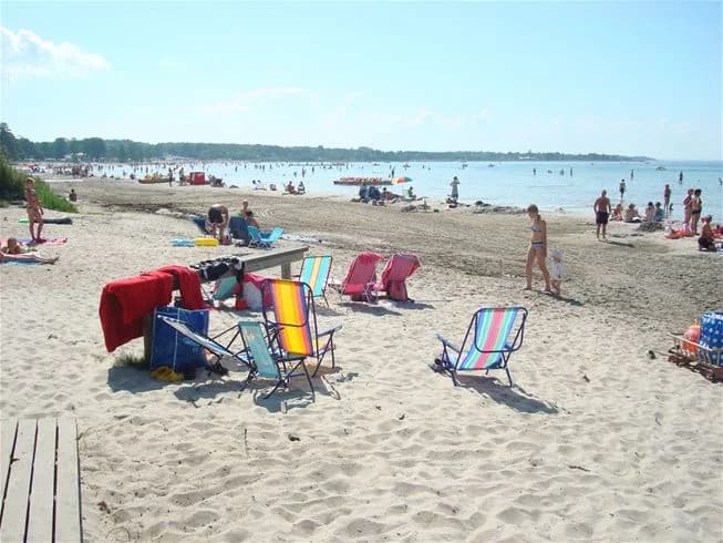 En solig sommardag med människor som solar och njuter på stranden vid Klinta camping, omgivet av vatten och sand.