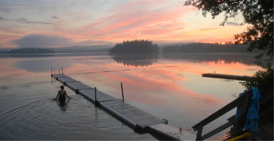 Solnedgång över vatten vid Sölje Camping, med en klar himmel och mjukt upplysta moln vid horisonten.