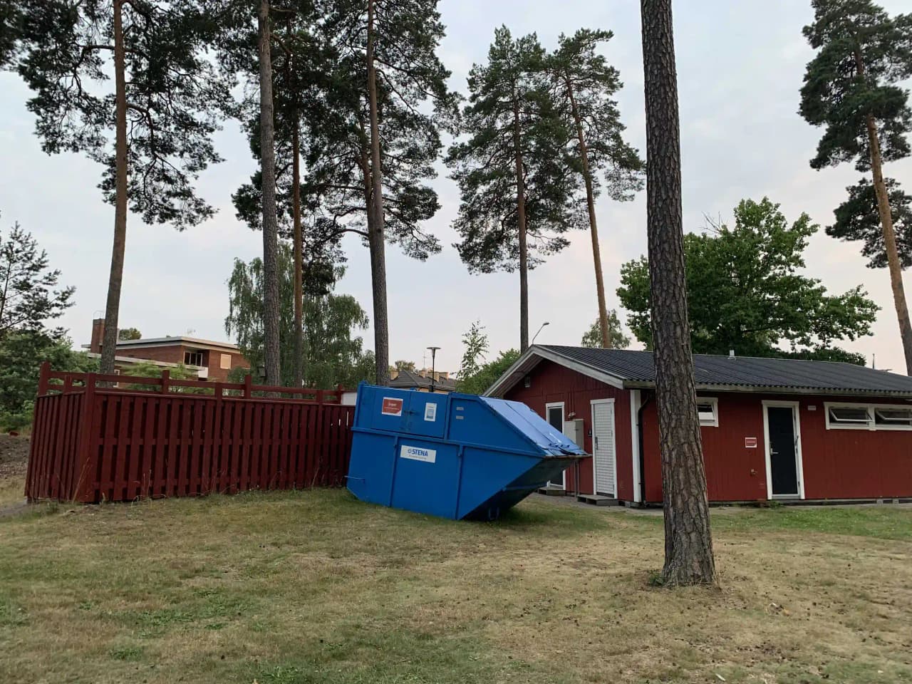 En campingplats med en liten byggnad, omgiven av grönska och en välskött gräsmatta.