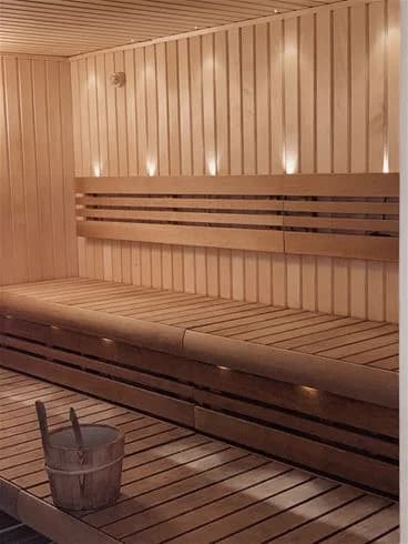 En inbjudande bastu med träpanel och träbänkar, glänsande golv av trä och ljust tak, vilket utstrålar en känsla av renhet och avkoppling.