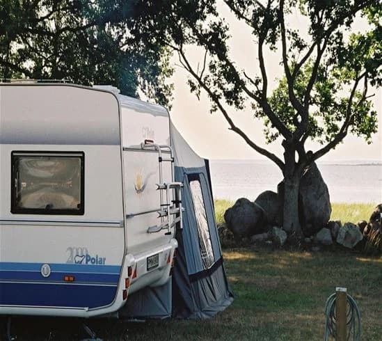En bild av Saxnäs camping som visar husbilar och husvagnar uppställda på en campingplats. Tält och en markis syns i bakgrunden, omgivna av träd och natursköna landskap.