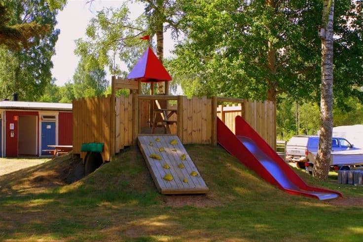 En lekplats med rutschkana och lekhus i en parkmiljö vid Otterbergets bad och camping.