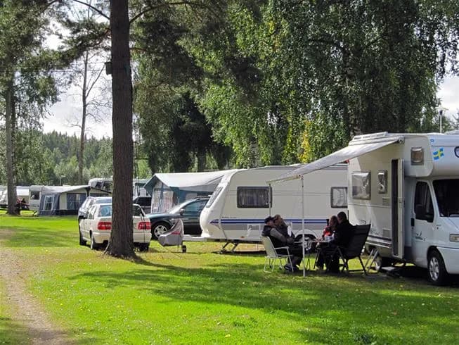 En campingplats där en husvagn står parkerad. I förgrunden syns en cykel lutad mot husvagnen. Området är öppet och verkar vara en del av Otterbergets bad och camping.