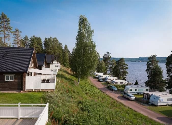 En naturskön vy över Leksand Resort med en kustlinje som möter en glittrande sjö, omgiven av frodiga grönområden och kuperad terräng.