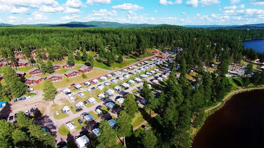 En naturskön vy vid Leksand Resort med träd som kantar sjön. Vattnet glittrar i solen, och det grönskande landskapet skapar en fridfull atmosfär perfekt för rekreation.