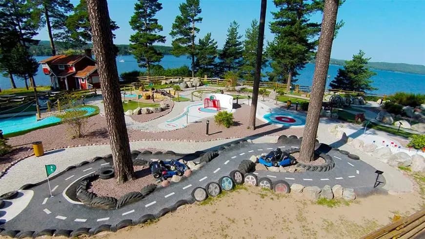 Alt-text: "Vacker anlagd park vid Leksand Resort med frodig grönska och stigar omgivna av träd och blommor."