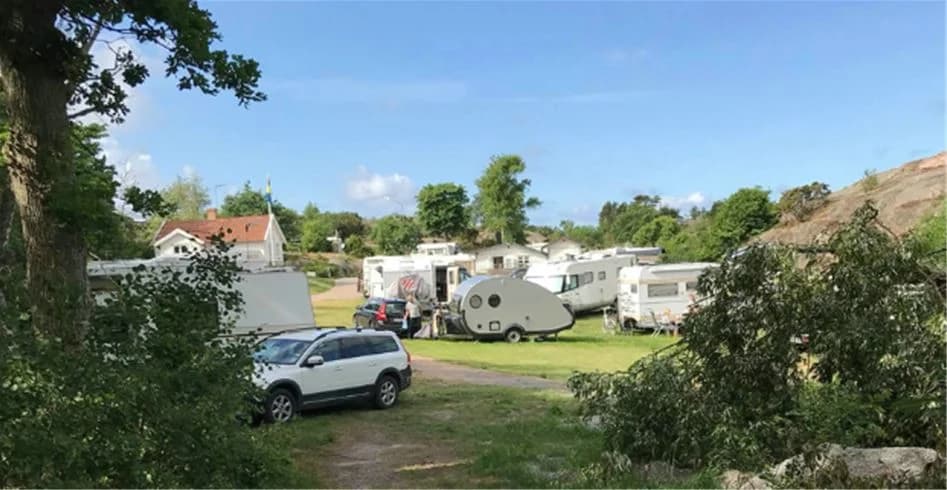 En idyllisk campingplats i Fjällbacka med parkerade husvagnar, en campingstuga och grönskande växtlighet. En husbil syns på uppfarten.
