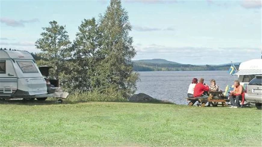 En husbil och en husvagn står uppställda på Munkebergs camping omgiven av grönska, med en sjö i bakgrunden.