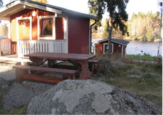 En trästuga med veranda omgiven av grönskande natur på Munkebergs camping.