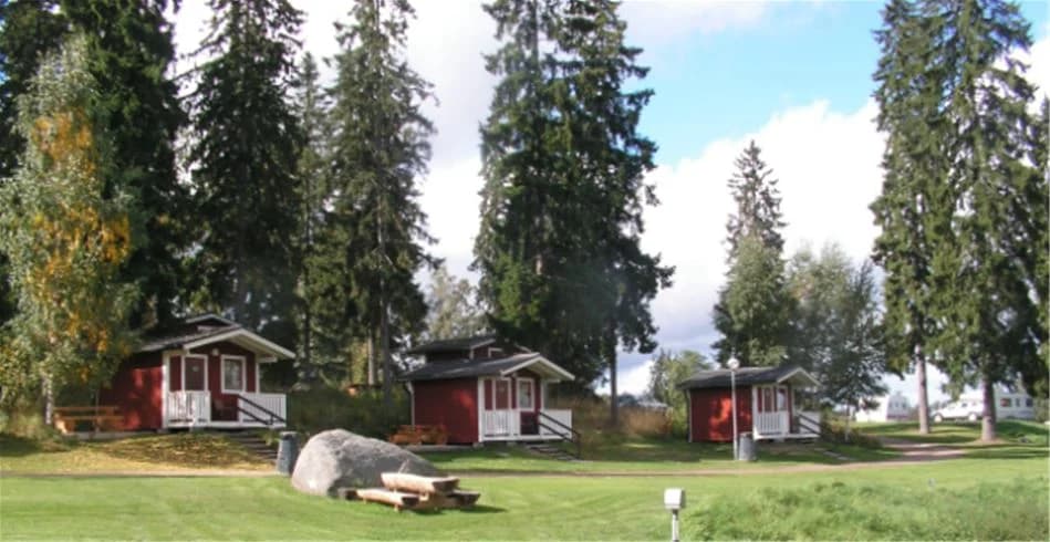 En grönskande campingplats med träd och gräsmattor omgivna av stugor och koniferer på Munkebergs camping.