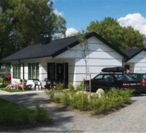 En bild av Gustavsvik Resort som visar ett pittoreskt hus med brunt tak och vita väggar, omgivet av en välskött gräsmatta och trädgårdsbyggnader.