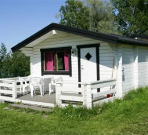 En vinterlandskap med ett timmerhus vid Gustavsvik Resort, omgiven av snö och träd, vilket skapar en mysig och inbjudande atmosfär.