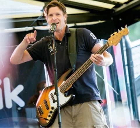 En gitarrist uppträder på scen med en akustisk gitarr på Gustavsvik Resort, omgiven av publikens energi och uppmärksamhet.