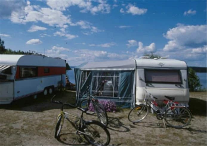 "Bilden visar campingplatsen Storsands Camping med uppställda husvagnar, husbilar och tält. Området är omgivet av grönska och skapandet och används för friluftsaktiviteter."