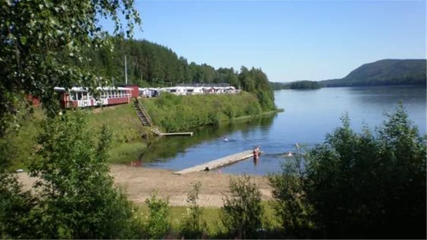 En naturskön vy över vattendrag och omgivande grönska vid Kävsta camping, med en stilla sjö eller flod omgiven av trädridåer och gräsbevuxna bankar under en klar himmel.