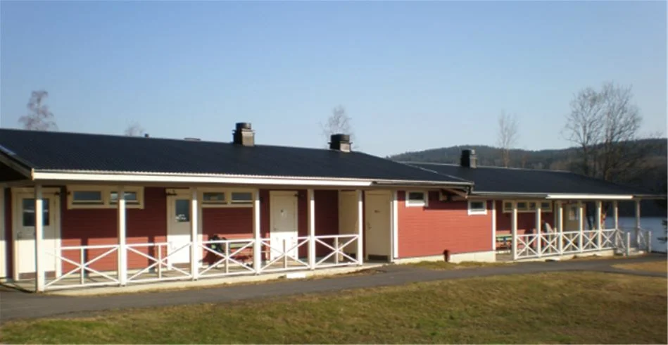 En charmig stuga med veranda och sluttande tak omgiven av grönska på Kävsta Camping.