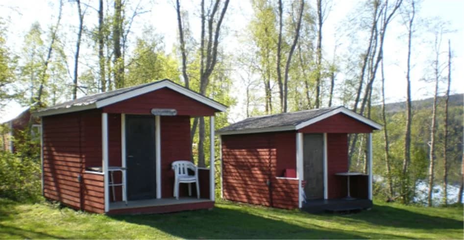 En liten stuga i trä med träpaneler och en mysig veranda, omgiven av frodig grönska på Kävsta Camping.