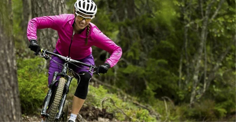En cyklist med hjälm och cykel på grusväg vid Idre Fjäll Camping, omgiven av grönskande natur.