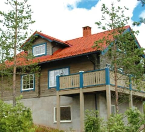 En träbyggnad med stora fönster och ett sluttande tak, omgiven av skogsmiljö. Byggnaden ser ut att vara en stuga eller ett fritidshus, typiskt för bostadsområden i natursköna områden som Orsa Grönklitt.