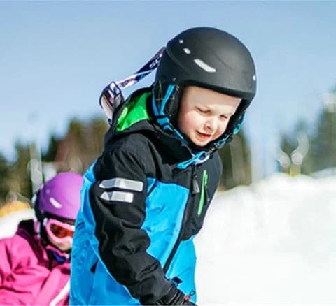 Ett barn klädd i vinterkläder, inklusive jacka, skidglasögon och hjälm, njuter av vintersport på Orsa Grönklitt.