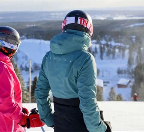 En person klädd i vinterkläder med skidutrustning står i ett snötäckt landskap på Orsa Grönklitt, redo för vintersportaktiviteter.