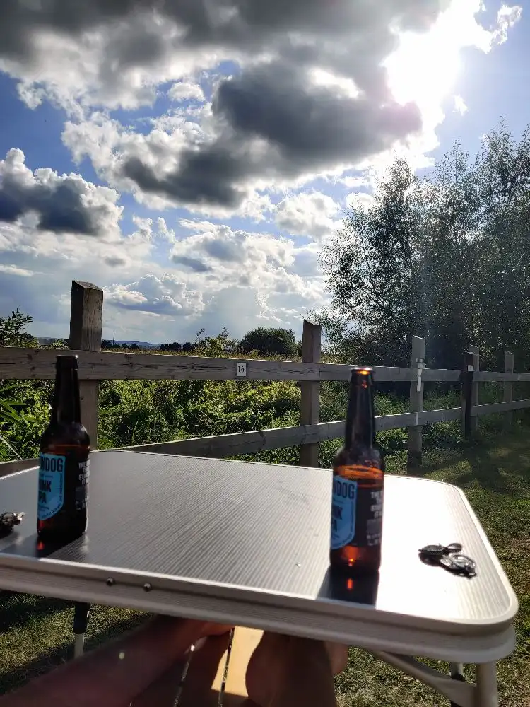 En picknickbänk vid Martins rökeri och camping med flera flaskor av alkoholhaltiga drycker, inklusive ölflaskor, placerade på bordet. Utomhusmiljö med utemöbler och ett somrigt intryck.