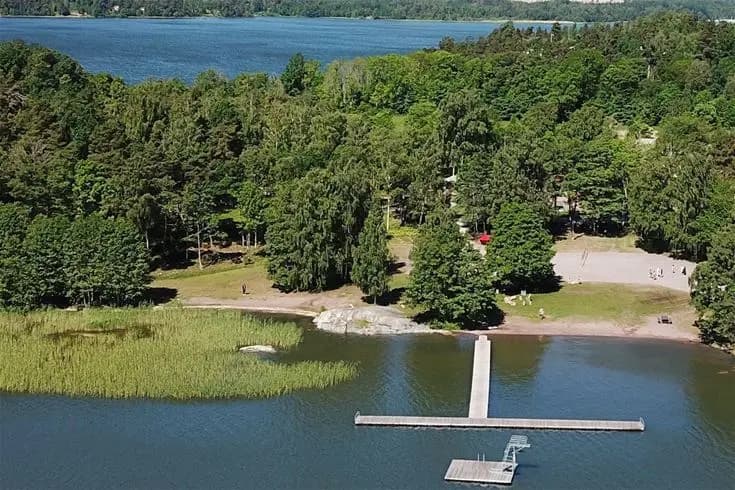 Flygfoto över Björknäs camping, naturskönt belägen vid en sjö med omgivande grönska och kustlinje.