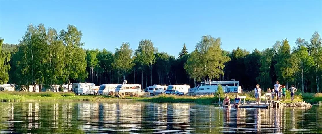 En campingplats vid en sjö med båtar, husvagnar och grönskande naturområde, idealisk för utomhusaktiviteter och avkoppling.