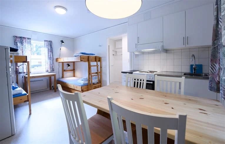 Bild av ett enkel möblerat rum på Östersunds camping, med trägolv och träinredning. Det finns våningssängar och stolar, tillsammans med träpaneler i taket.