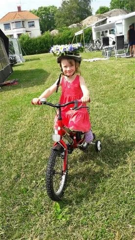 Ett barn cyklar glatt på en rosa cykel vid Wiggersviks camping, omgiven av somrig natur och barnvänliga aktiviteter.