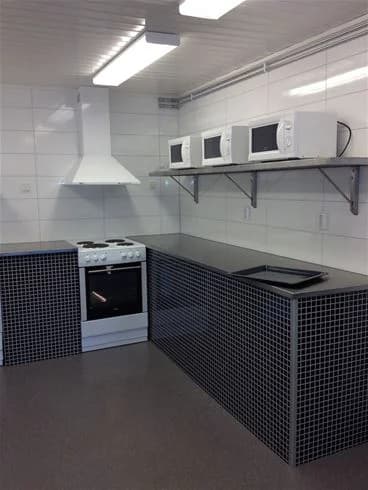 Ett modernt kök på Wiggersviks camping med köksbänk, spis och kylskåp. Golvet är ljust och rummet har ett luftigt och välorganiserat intryck.