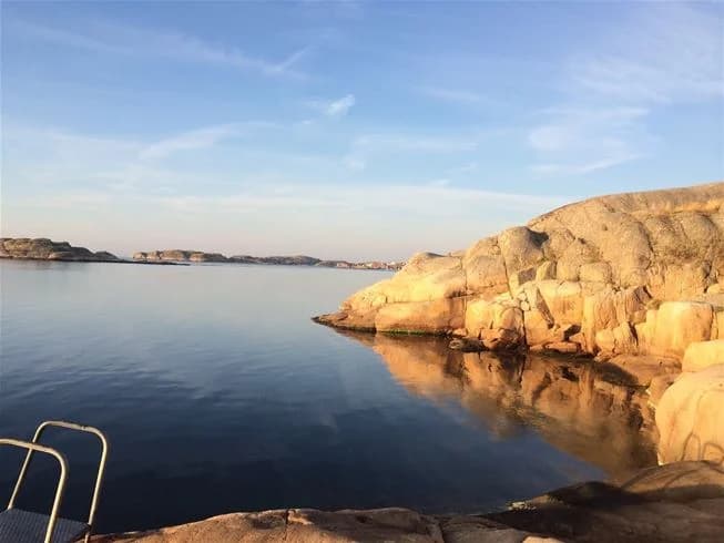 Vy över Wiggersviks camping med vatten i förgrunden, omgivet av klippiga kuster och en horisont i bakgrunden.