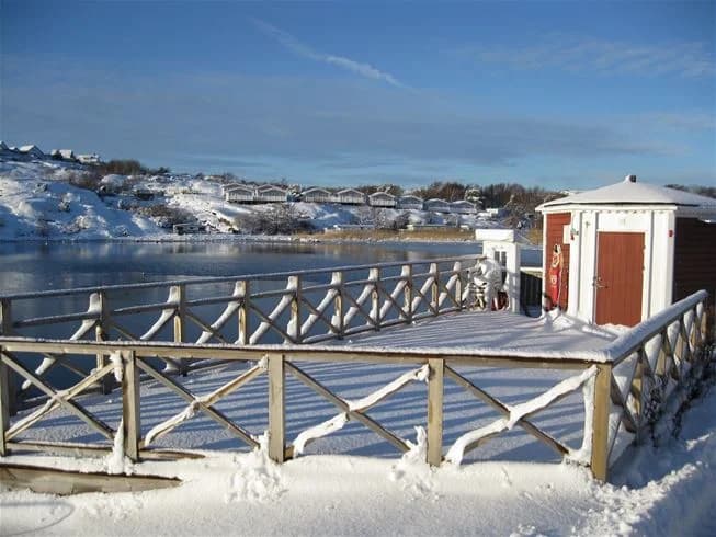 En vintervy över Wiggersviks camping med snötäckt mark och is. Ett räcke kantar platsen, och frost täcker omgivningen.
