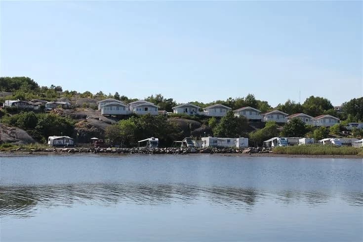 Bild av Wiggersviks camping med utsikt över en kustlinje. Sandstranden kantas av klippor och grönskande terräng. En vik breder ut sig i bakgrunden, med stilla vatten där den möter himlen. En populär destination vid havet.