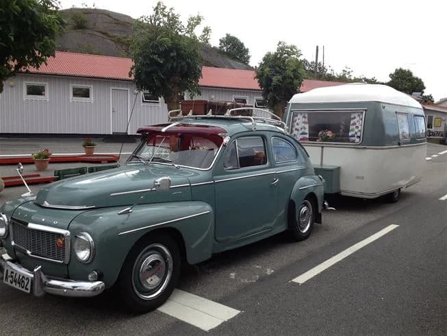 En Volvo PV444 står parkerad på Wiggersviks camping, omgiven av grönska och campingmiljö.